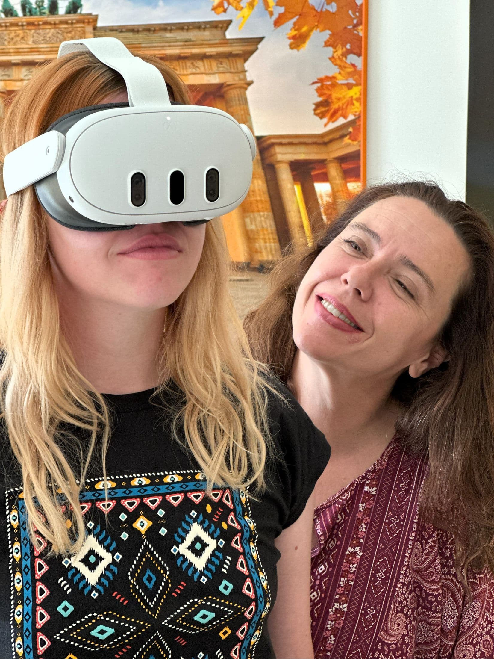 A teacher in a headset with a colleague leaning in beside her